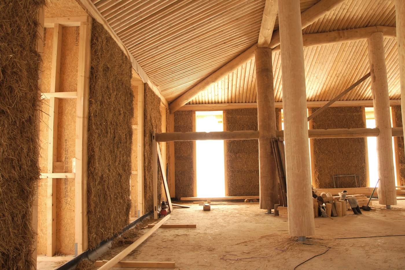 Ein Strohballenhaus – hier mit lasttragenden Holzstammstützen – von innen. Die Wände werden mit Lehm verputzt.  (Bild Atelier Schmidt)
