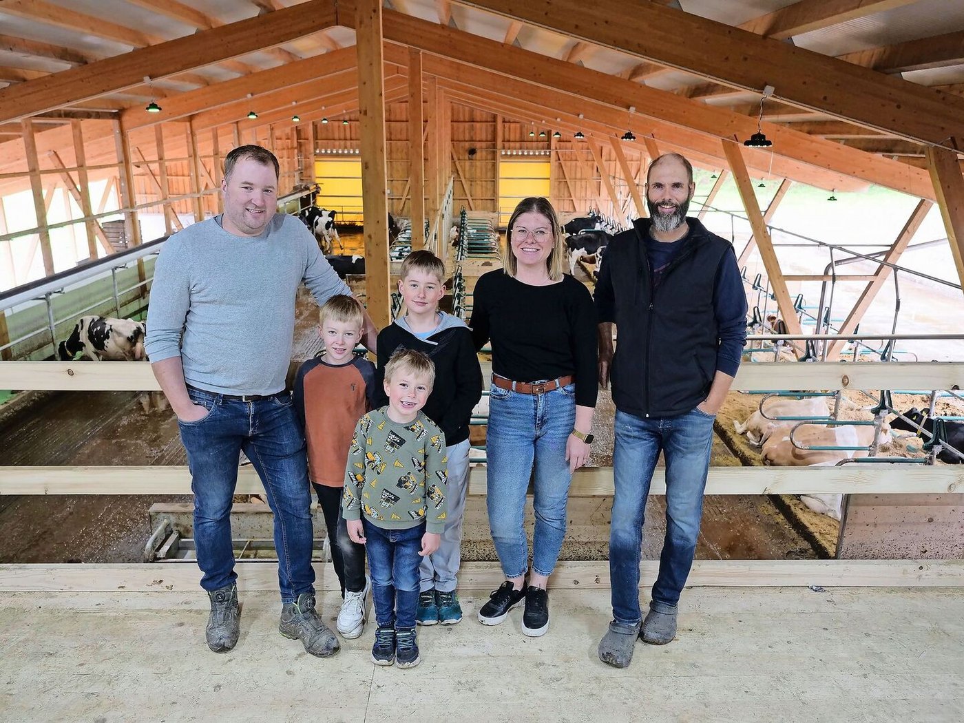 Martin und Andrea Blaser mit ihren Kindern Niklas, Magnus und Linus sowie Markus Schafroth (v. l. n. r.) in ihrem neu gebauten Stall. Ganz links ist das obenliegende Futterband zu sehen.
