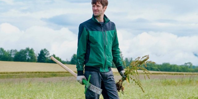 Kilian Baumann steht in Arbeitskleidung auf einem Feld.