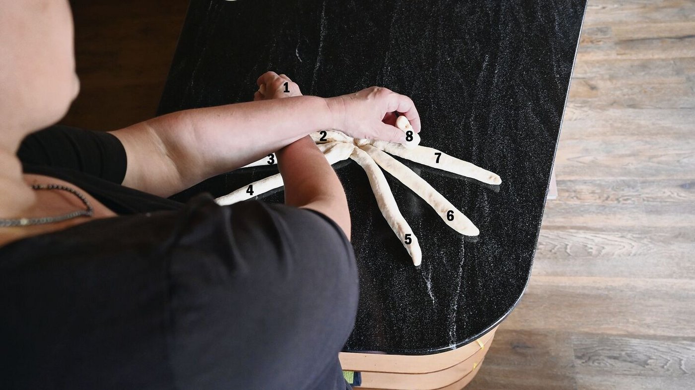 Mit der rechten Hand Strang 1 nehmen, die linke Hand nimmt Strang 8, Stränge kreuzen.