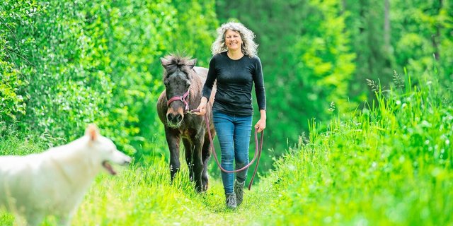 Neben einer der Hecken, die zum Betrieb gehören, spaziert Corinne Kählin mit ihrer alten Stute Dögg. Im Vordergrund die Hündin Dis, eine der sieben Hunde, die auf dem Hof alt werden dürfen.
