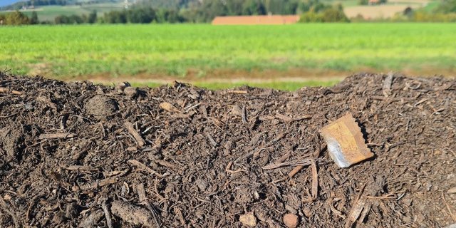 An einer Kompostmiete am Feldrand sind diverse Verpackungen und Fitzelchen von Plastik zu sehen.