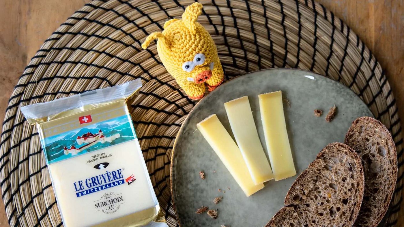 Das gestrickte Migros-Maskottchen posiert vor Käse, der beim Detailhändler nun günstiger zu haben ist. (Bild Migros)