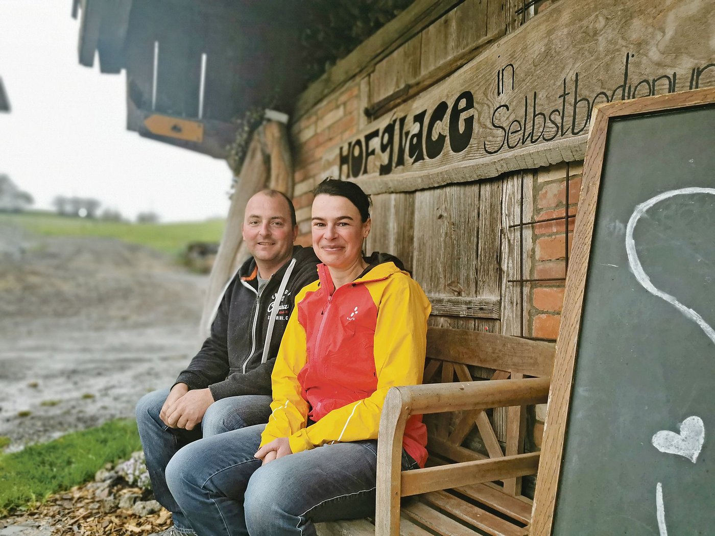 In Regenjacken sitzen Daniel Krähenbühl und Silvia Gerber auf dem Bänklein vor ihrem Hofladen. Hier verpflegen sich an sonnigen Tagen Wanderer mit der hausgemachten Glace aus der hofeigenen Milch. (Bilder Simone Barth)