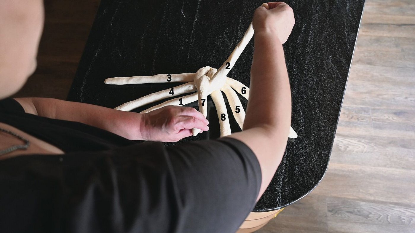 Rechte Hand unter linkem Arm hindurchgreifen und Strang 2 holen, kreuzen. Linke Hand legt Strang 7 neben Strang 8 ab. 