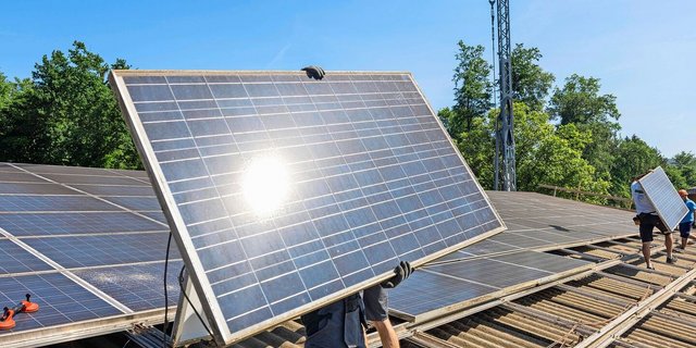 Ein Monteur trägt ein Solar-Panel, das er auf dem Dach montieren will.